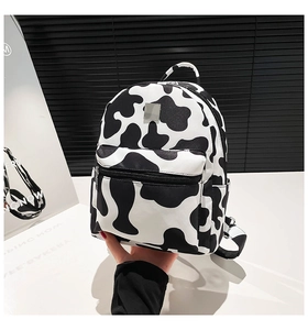 Detail view of mini cow-print backpack with a front zipper pocket and top white handle