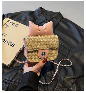 Detailed view of pink leather bow and metal flower clasp on a mini straw crossbody bag