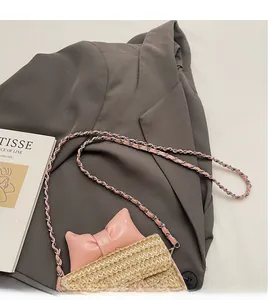 Detail of a mini straw woven crossbody bag featuring a pink bow and metal chain strap