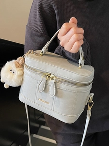Elegant light gray vanity case handbag with plush monster charm and adjustable strap