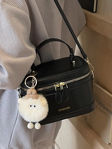 Fashionable black box-shaped crossbody bag with gold hardware and a white plush charm