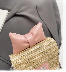 Detail of a mini straw woven crossbody bag featuring a large pink leather bow and metal clasp