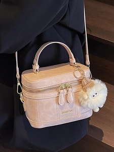 Fashionable beige box-shaped crossbody bag with gold hardware and plush charm accessory