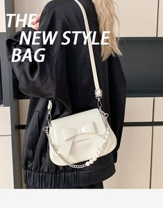 Detail of cream-colored crossbody bag with bow decoration and pearl chain on a model