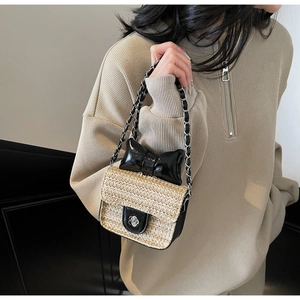 Detail of a mini straw woven bag with a black leather bow and flower buckle on a chain strap