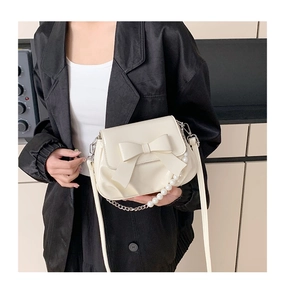 Detail of a creamy white bow crossbody bag with pearl handle and polished leather finish