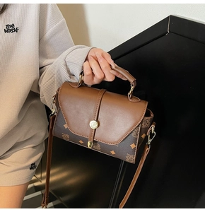 Close-up of brown monogrammed square bag with golden round metal clasp and vintage texture