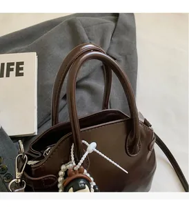 Dettaglio della borsa marrone in pelle cerata con ciondolo a perla e chiusura a zip