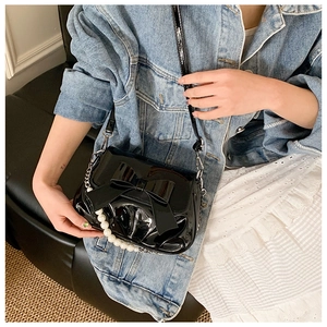 Detail of black patent leather crossbody bag with bow decoration and pearl strap