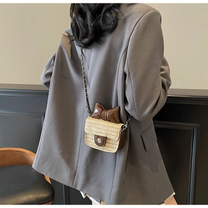Detail of a mini straw square bag featuring a brown bow and flower metal clasp