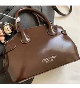 Dettaglio borsa in pelle cerata color caffè con logo MIKAXIQI in metallo e ciondolo di perle