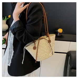 Straw woven tote bag with brown leather strap worn by a model in a minimalist setting