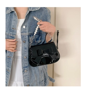 Detailed view of the black patent leather handbag featuring a large bow and pearl chain strap