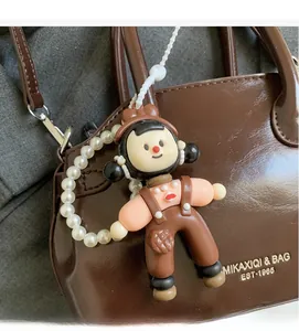Ciondolo bambola marrone con catena di perle su borsa in pelle cerata per stile casual