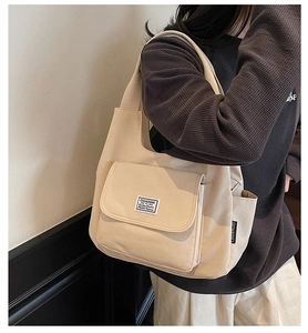 Detail of canvas tote bag showing front flap pocket and woven brand label in light beige color