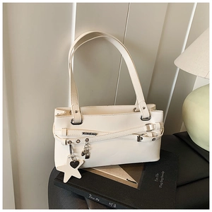 Détail d'un sac porté épaule minimaliste beige avec finitions argentées et breloques