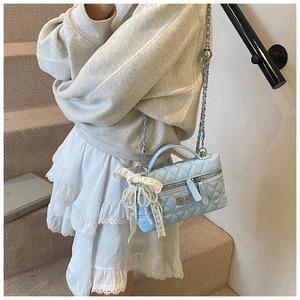 Detail of light blue quilted crossbody bag featuring pearl bow charm and silver chain