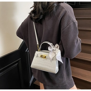 Détail d'un sac à main gris clair embossé croco avec fermoir doré et foulard en soie