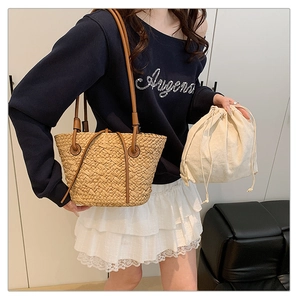 Detail view of woven straw tote bag with brown leather straps and drawstring canvas liner bag