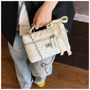 Close-up of white quilted mini bag with lace pearl bow charm and silver chain strap