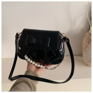 Detailed macro view of a black glossy handbag featuring a large bow and pearl chain strap