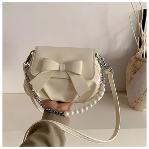 Detail of cream bow shoulder bag with decorative pearl handle and metal chain strap
