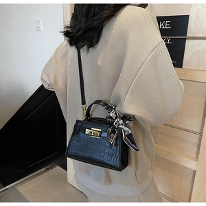 Détail d'un sac à main noir motif crocodile avec foulard en soie et fermoir métallique