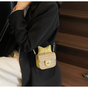 Detail shot of a yellow woven mini crossbody bag with a large bow on a dark blazer