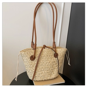 Detail of hand-woven straw tote bag with brown leather shoulder straps and drawstring closure