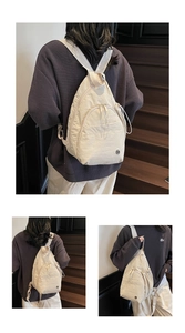 Vue détaillée d'un sac à dos beige léger en tissu avec un logo métallique circulaire