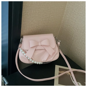 Detail shot of a sweet pink patent leather crossbody bag with a large bow and pearl chain