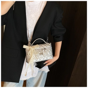 Silver quilted crossbody bag with lace bow charm shown worn on a black and white outfit