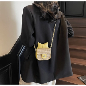 Detail of a yellow straw mini crossbody bag with a large bow and flower buckle on a chain
