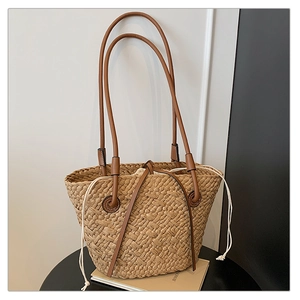 Detailed close-up of straw woven tote with brown leather handles and white canvas drawstring