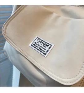 Detail of off-white canvas shoulder bag with fine stitching and brand label on flap