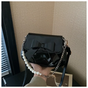 Detail of black patent leather bag with large bow and pearl chain strap accents