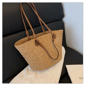 Detail of hand-woven straw tote bag with leather strap on a black leather seat