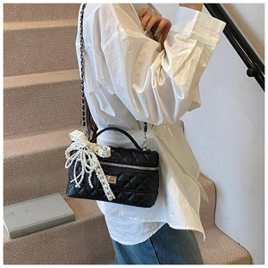 Close-up of black quilted leather crossbody bag with a white pearl woven bow decoration