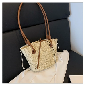Close-up of beige woven straw tote bag featuring brown leather shoulder straps and drawstring