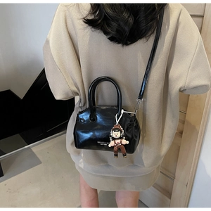 Dettaglio della borsa in pelle nera lucida con scritte bianche e ciondolo a forma di bambina