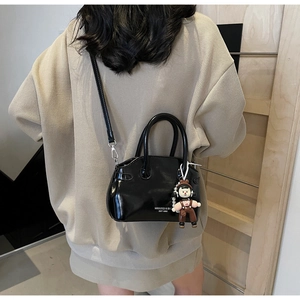 Dettaglio borsa in pelle cerata nera con ciondolo a bambola su maglione beige