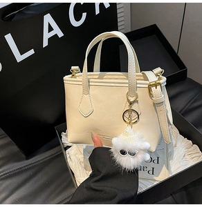 Close-up of cream mini bucket bag with gold hardware and plush charm in a gift box