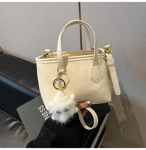 Detail of off-white faux leather bucket bag with plush monster charm and top handles