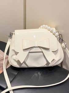 Elegant cream white bow crossbody bag with pearl chain handle on a sleek surface