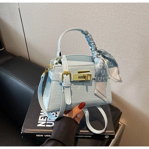 Détail du sac à main bleu clair effet croco avec fermoir doré et foulard en soie