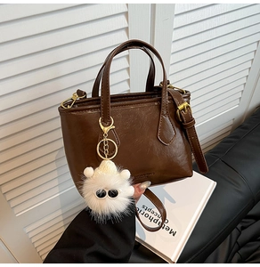 Detailed view of deep brown vintage crossbody bag with a cute white plush monster charm
