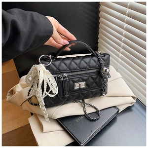 Detail of black quilted leather handbag with pearl bow charm and chain strap