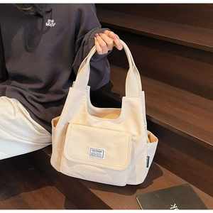 Close-up of off-white canvas shoulder bag with front flap pocket and woven brand label