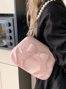 Pink crossbody bag with large bow and pearl chain strap in a lifestyle setting