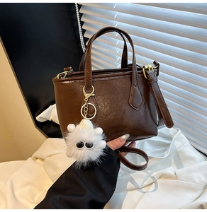 Detail of dark brown leather mini bucket bag featuring a white plush monster charm